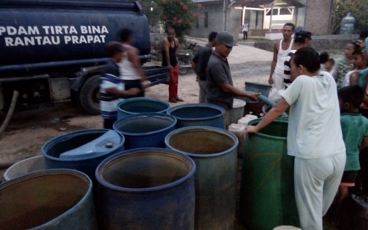 Kades Kampung Baru saat memegang selang menuangkan air bersih ke drum untuk warga