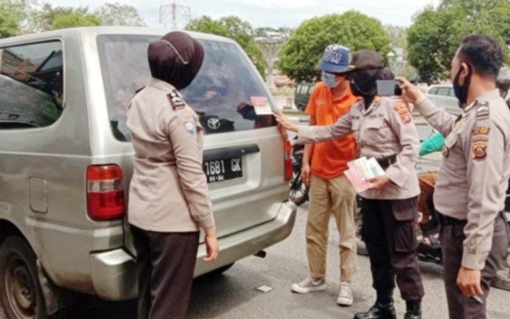 Personel Polres OKU Timur memberikan imbauan sekaligus pasang stiker di mobil pengendara yang melintas