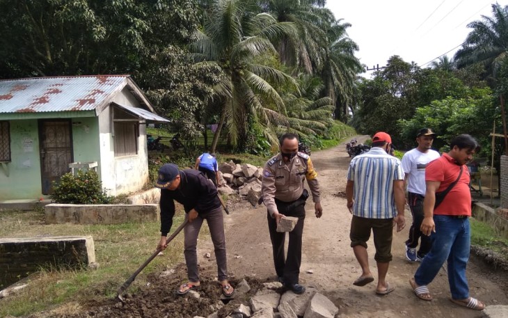Bhabinkamtibmas Gotong Royong Bersama Warga Timbun Jalan Berlubang