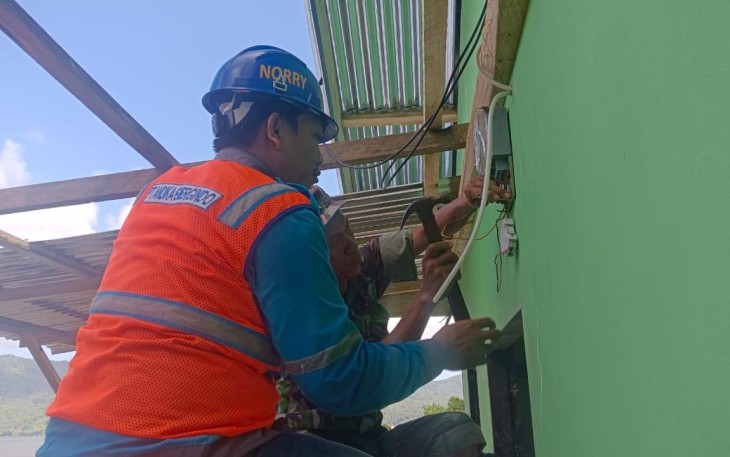 Satgas TMMD bersama pegawai PLN saat memasang instalasi listrik