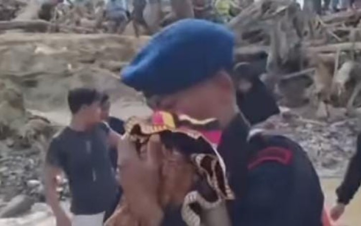 Seorang anggota Brimob terlihat menggendong seorang bayi menyeberangi jembatan darurat yang hampir roboh diterpa derasnya arus sungai pascabanjir.