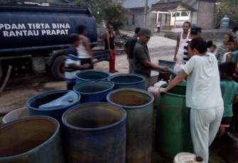 Kades Kampung Baru saat memegang selang menuangkan air bersih ke drum untuk warga