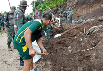 Personil kodim 1310/Bitung bersama warga saat membersihkan jalan yang tertimpa tanah longsor