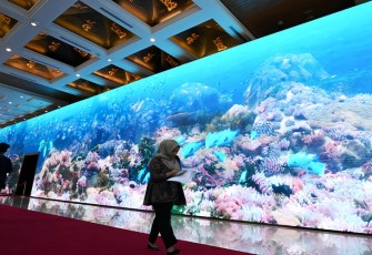 Seorang perempuan berjalan melewati monitor yang menampilkan ekosistem laut di venue HLM AIS Forum 2023 di Bali Nusa Dua Convention Center, Kabupaten Badung, Bali, Senin (9/10/2023). Monitor berukuran panjang 79 meter dan tinggi 6 meter yang menampilkan animasi ekosistem bawah air karya animator lokal ini akan menyambut kedatangan delegasi HLM AIS Forum 2023 di venue. Media Center HLM AIS Forum 2023/Akbar Nugroho Gumay/pras/ratih.