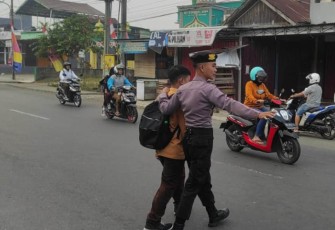 Petugas saat menyeberangkan anak sekolah