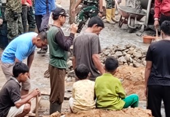 Salah satu personel Satgas TMMD Prada Bayu bekerja sambil bermain bersama anak-anak