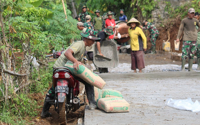 Sulitnya titik lokasi pengecoran jalan, memaksa prajurit melangsir material semen menggunakan sepeda motor.