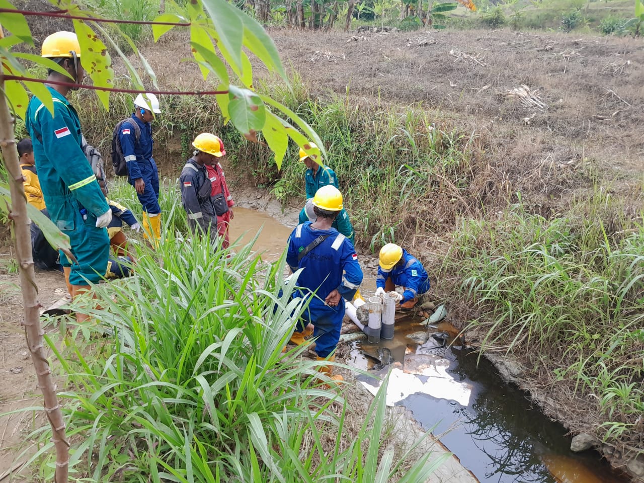 Para pekerja sedang melokalisir sungai dengan sistem sifon untuk memisahkan air dan minyak.