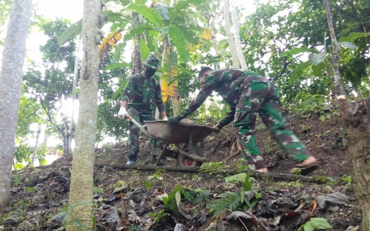 Dua Anggota Satgas TMMD Saling Kerjasama dalam Pengedropan Batu Bahan MCK Umum