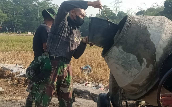 "Anggota Satgas TMMD sedang menuang bahan material ke dalam Molen pengaduk semen"