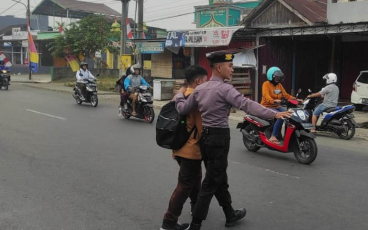 Petugas saat menyeberangkan anak sekolah