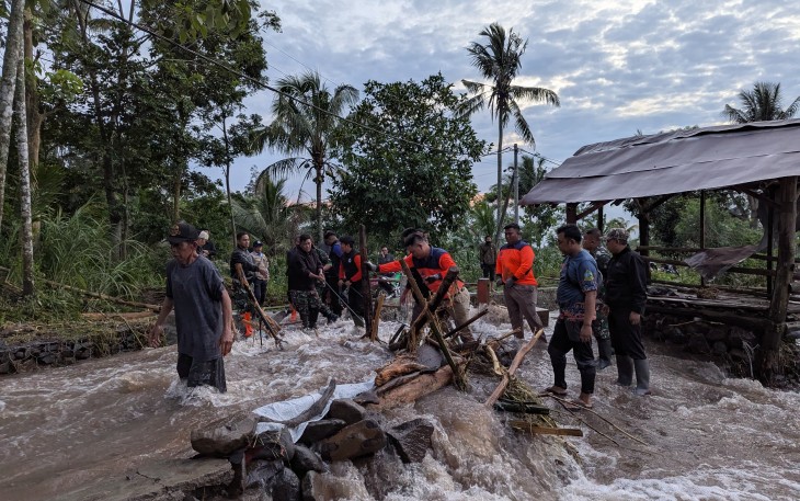 Tim gabungan membersihkan material kayu yang menyumbat jembatan desa akibat banjir bandang menerjang Desa Gunungsari, Kabupaten Bondowoso