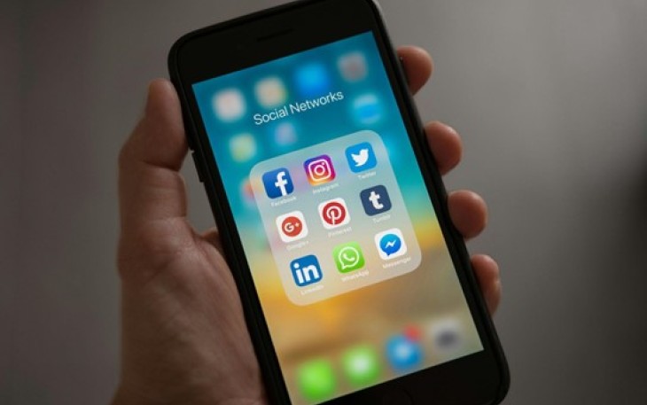 Ilustrasi tangan menggenggam handphone dengan layar yang  menampilkan platform media sosial.  Foto: Pexels/Tracy Le Blanc