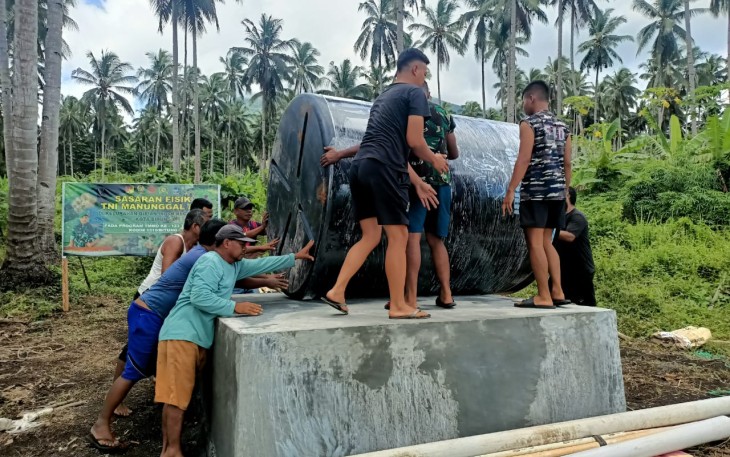 Satgas TMMD bersama warga saat meletakan material tong air berukuran 5.000 ton ke atas bak