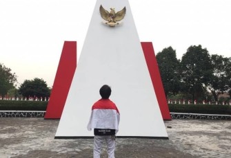 Seorang Pria diselimuti Bendera Merah Putih Berdiri di depan Monumen Taman Makam Pahlawan Seribu Serpong, Tangerang Selatan, Kamis (15/8/2019). Foto: Adhimas Kevin