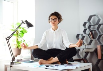 Seorang wanita bermeditasi di atas meja kantor (Foto: Freepik/cookie_studio)
