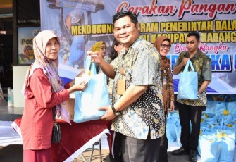 Dirut PUD Aneka Usaha, Samidi, menyerahkan paket sembako kepada salah satu warga dalam bazar pangan murah di halaman kantor PUD Aneka Usaha, Tasikmadu, Karanganyar, Selasa (26/3/2024)