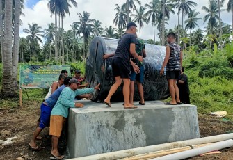 Satgas TMMD bersama warga saat meletakan material tong air berukuran 5.000 ton ke atas bak
